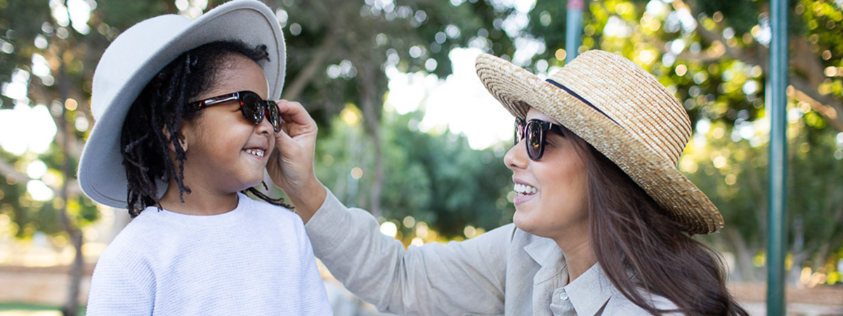 A young woman and a young boy together in the playground wearing sun protection