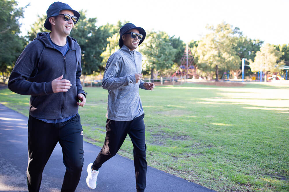 Two young men running in the park wearing sun protection