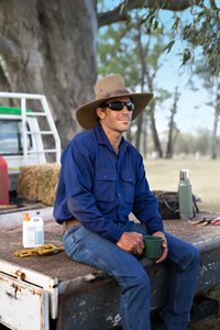 A farmer in sun protection sitting on the back of his ute enjoying a cuppa