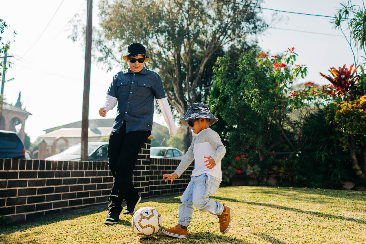 Image: A teenage boy and younger boy play soccer in the yard