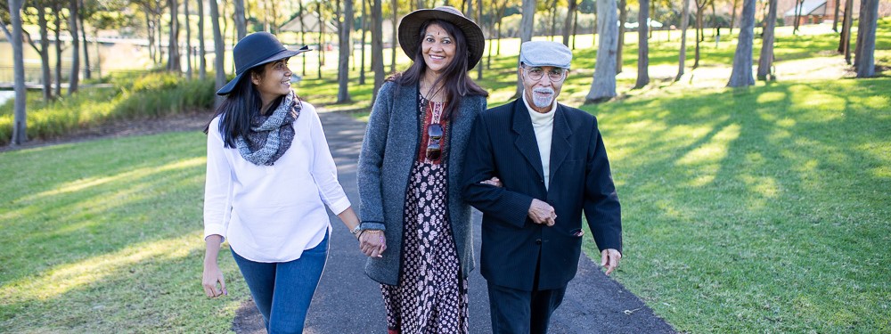 Three individuals wearing hats walking through a park on a sunny day